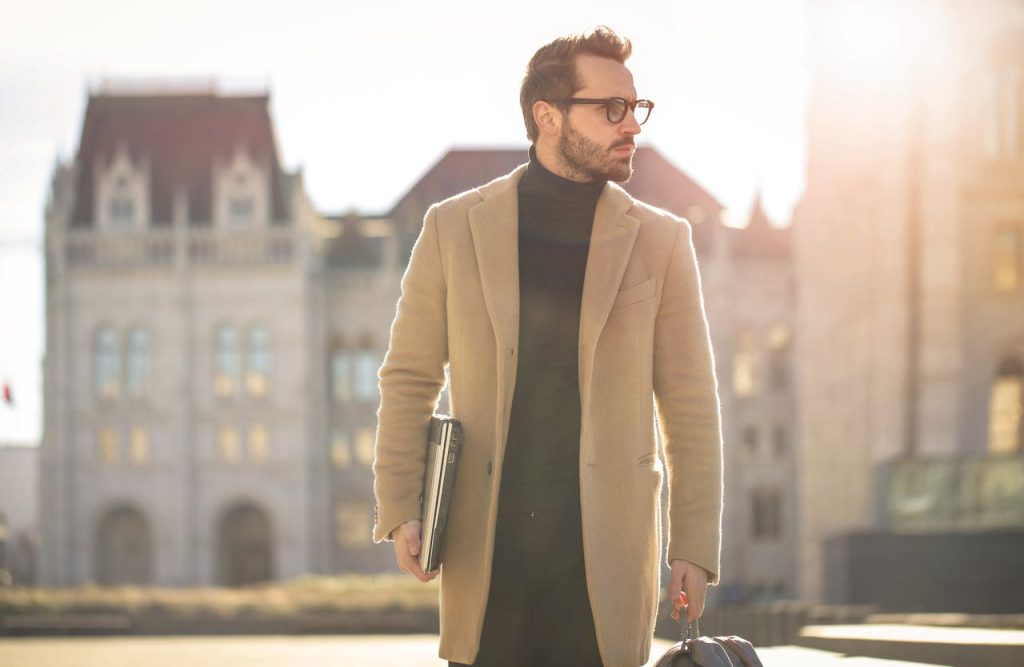Fashionable young man with a laptop walking in the sunlight near a historic building in Budapest.